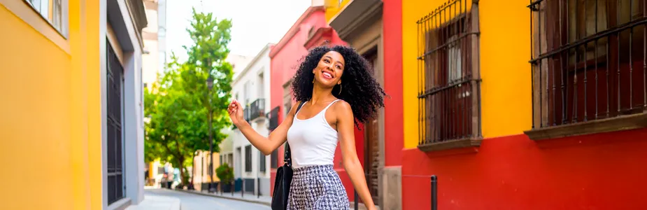 Mulher jovem brasileira usando look casual com regata e saia curta, em fundo colorido com amarelo, vermelho e preto.
